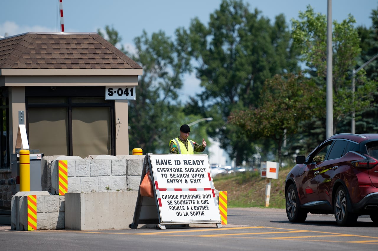 A soldier in uniform motions a car to move forward at a gate.