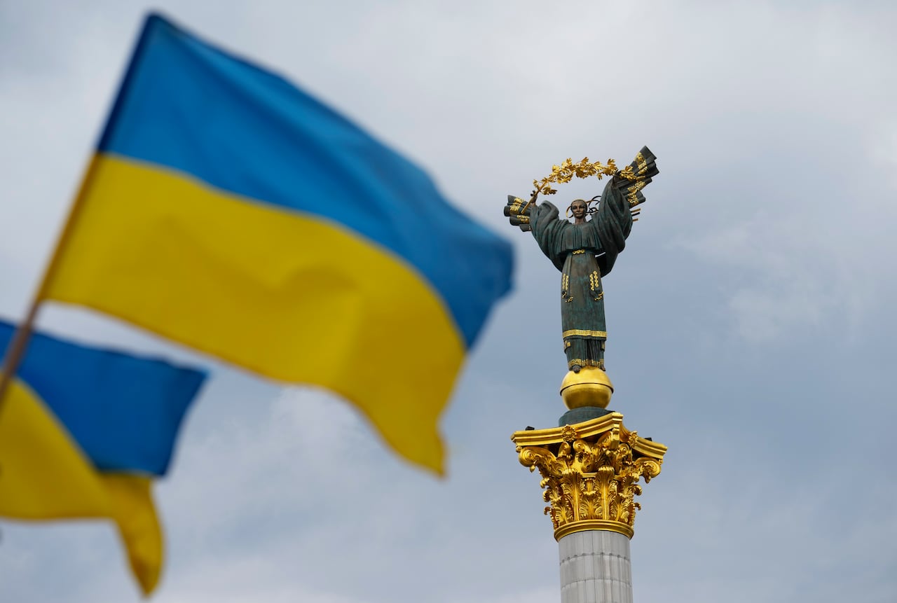 A Ukrainian flag waves in front of a monument.
