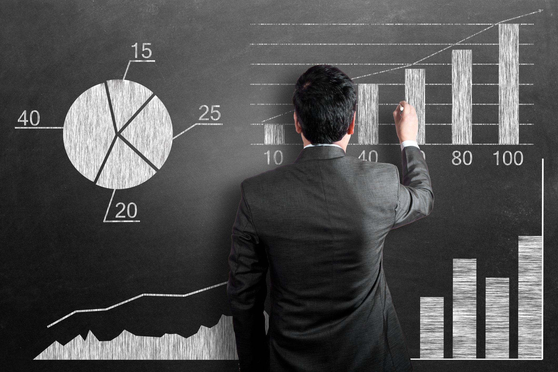 A person in a black suit draws stock-price charts on a blackboard.