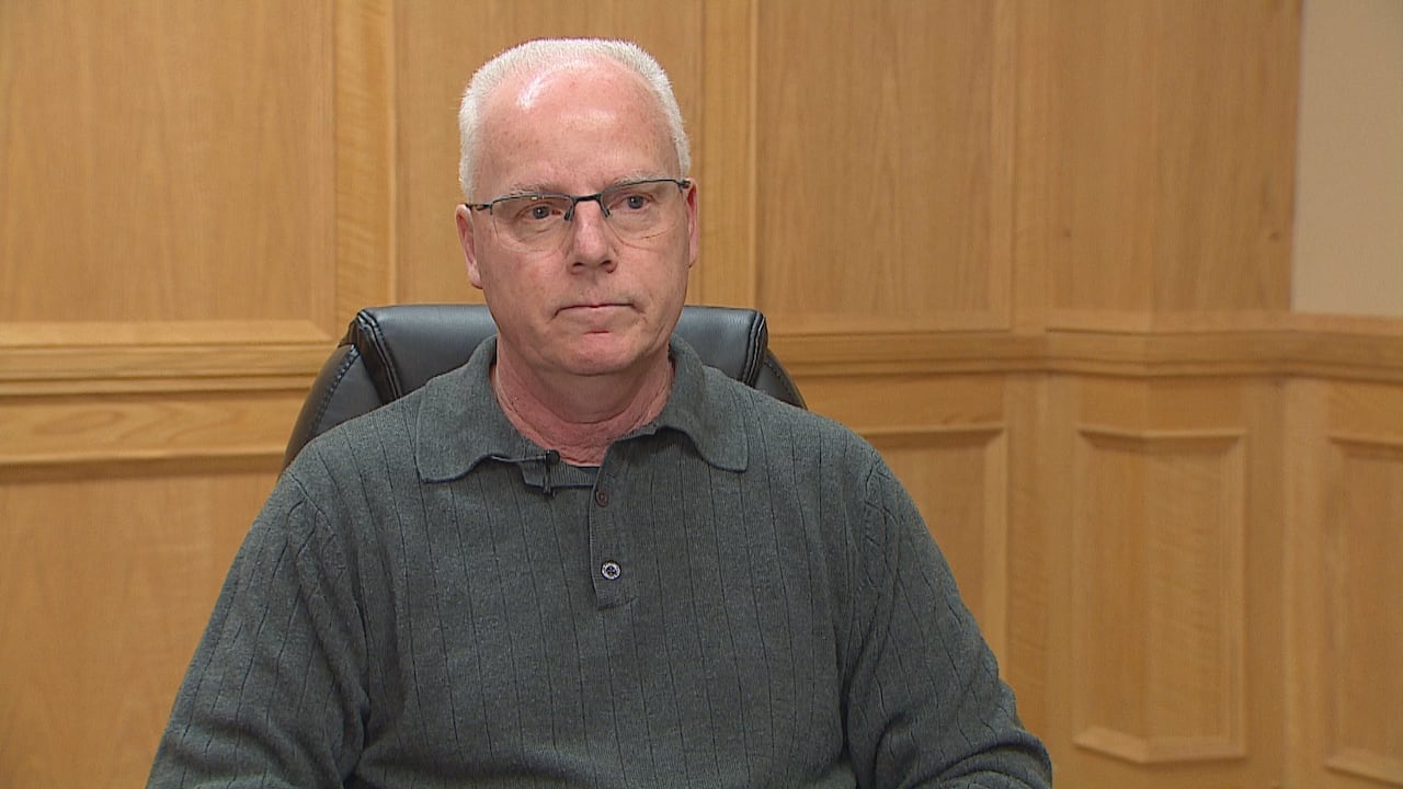 A man sits in a chair in front of a wall.