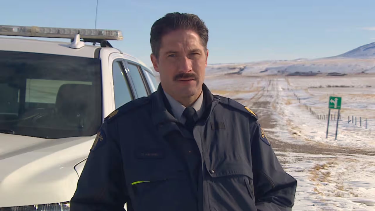 A man stands in a field in front of a vehicle.