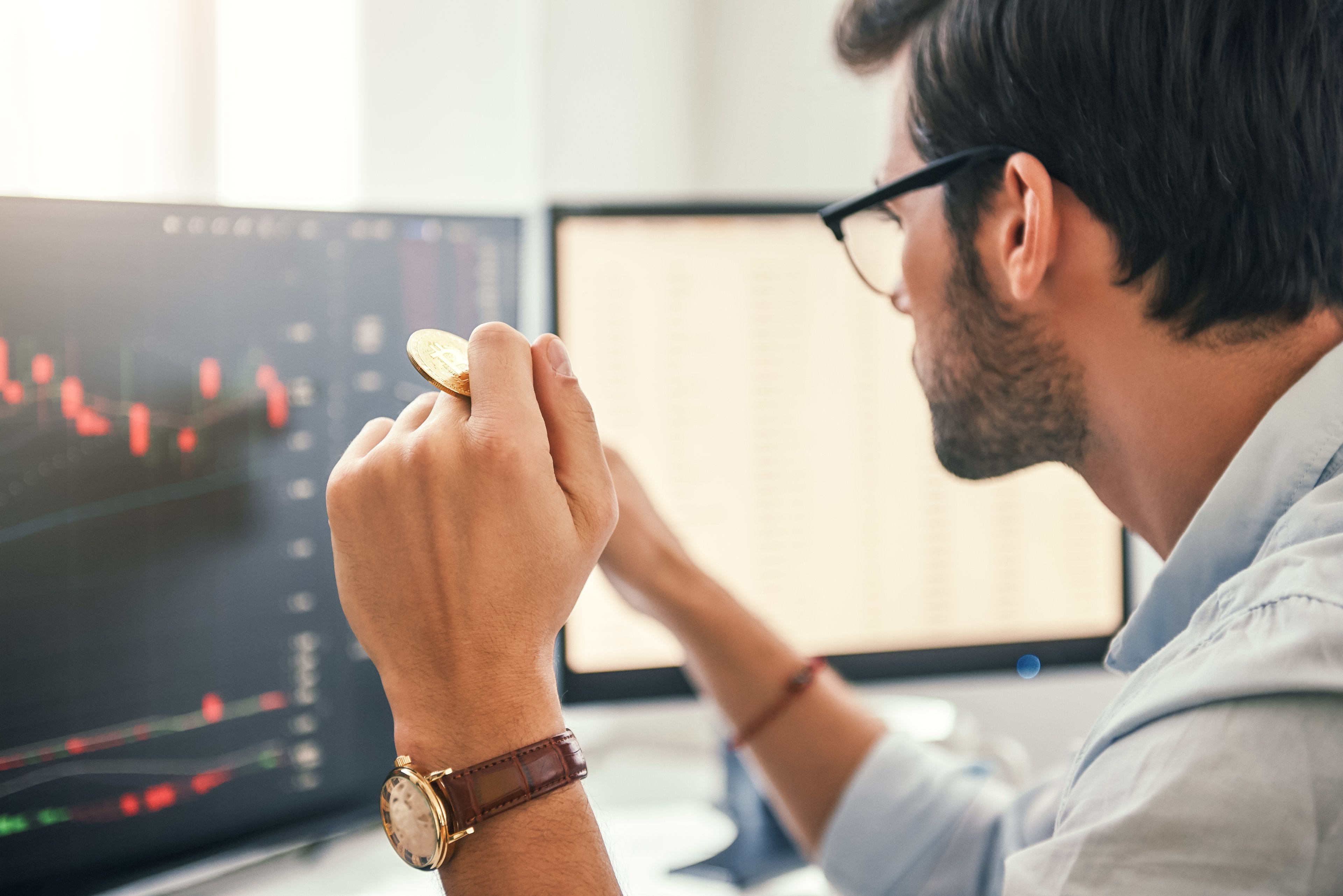 Investor looking at cryptocurrencies on their computer while holding a gold coin between their fingers. 