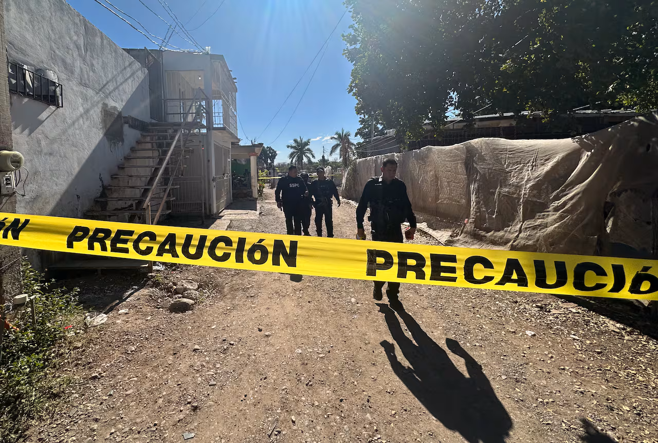 Three police officers walk up a driveway with caution tape strung across the entrance.