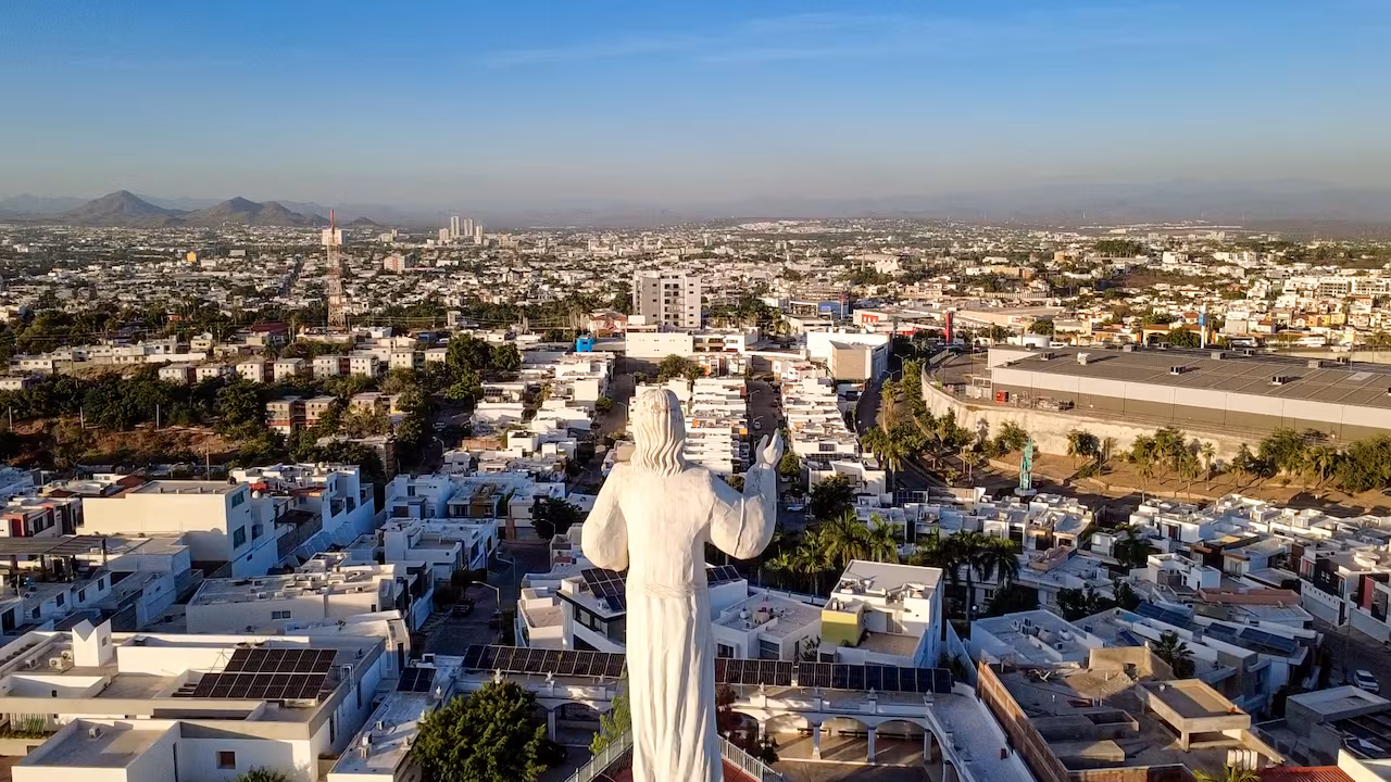 A city is spread to the horizon infront of a large statue that is built on a high point.