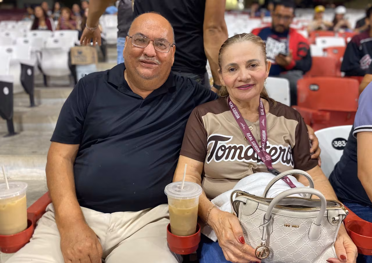 A man sits next to a woman wearing a baseball jersey with the world "Tomateros" on the front. 