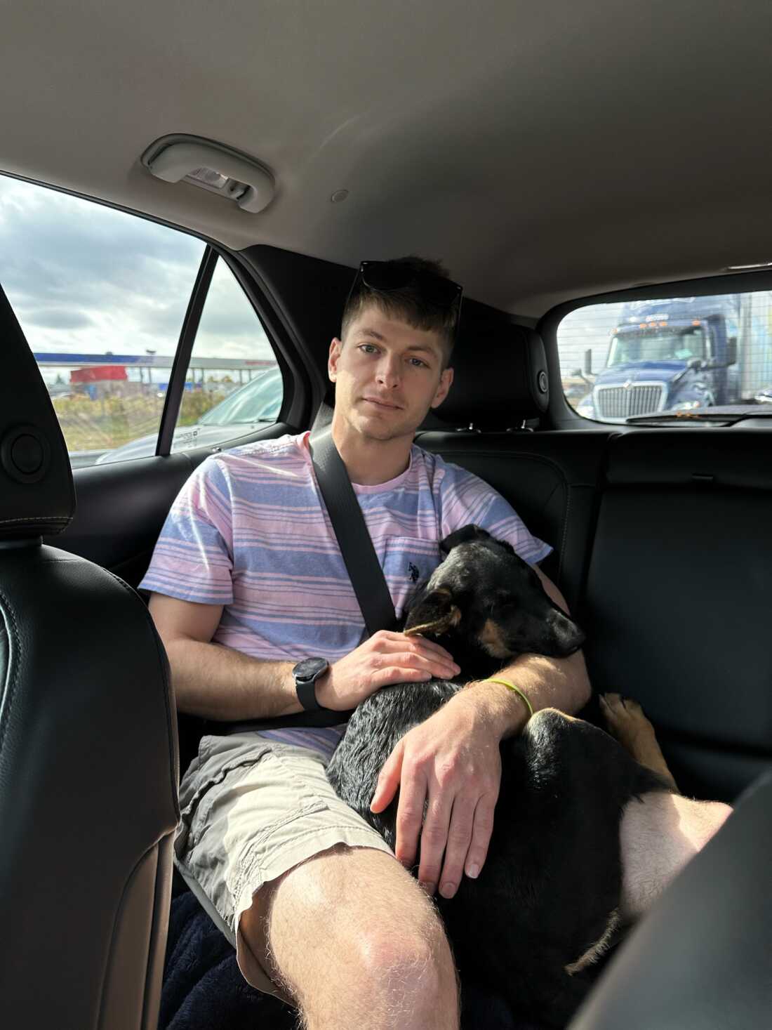 Patrick Heltzel is shown in the backseat of a car, cuddling a black dog. 