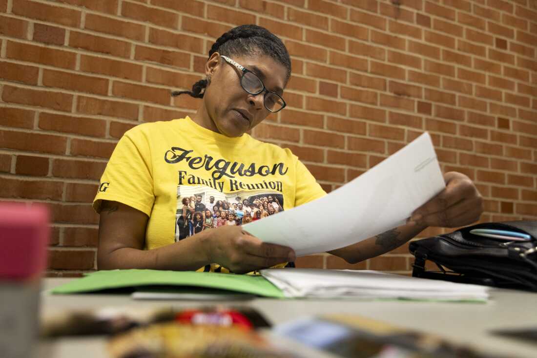 Tyeesha Ferguson sits at a table and wears reading glasses as she looks through various paperwork relating to her son, Quincy Jackson III. 