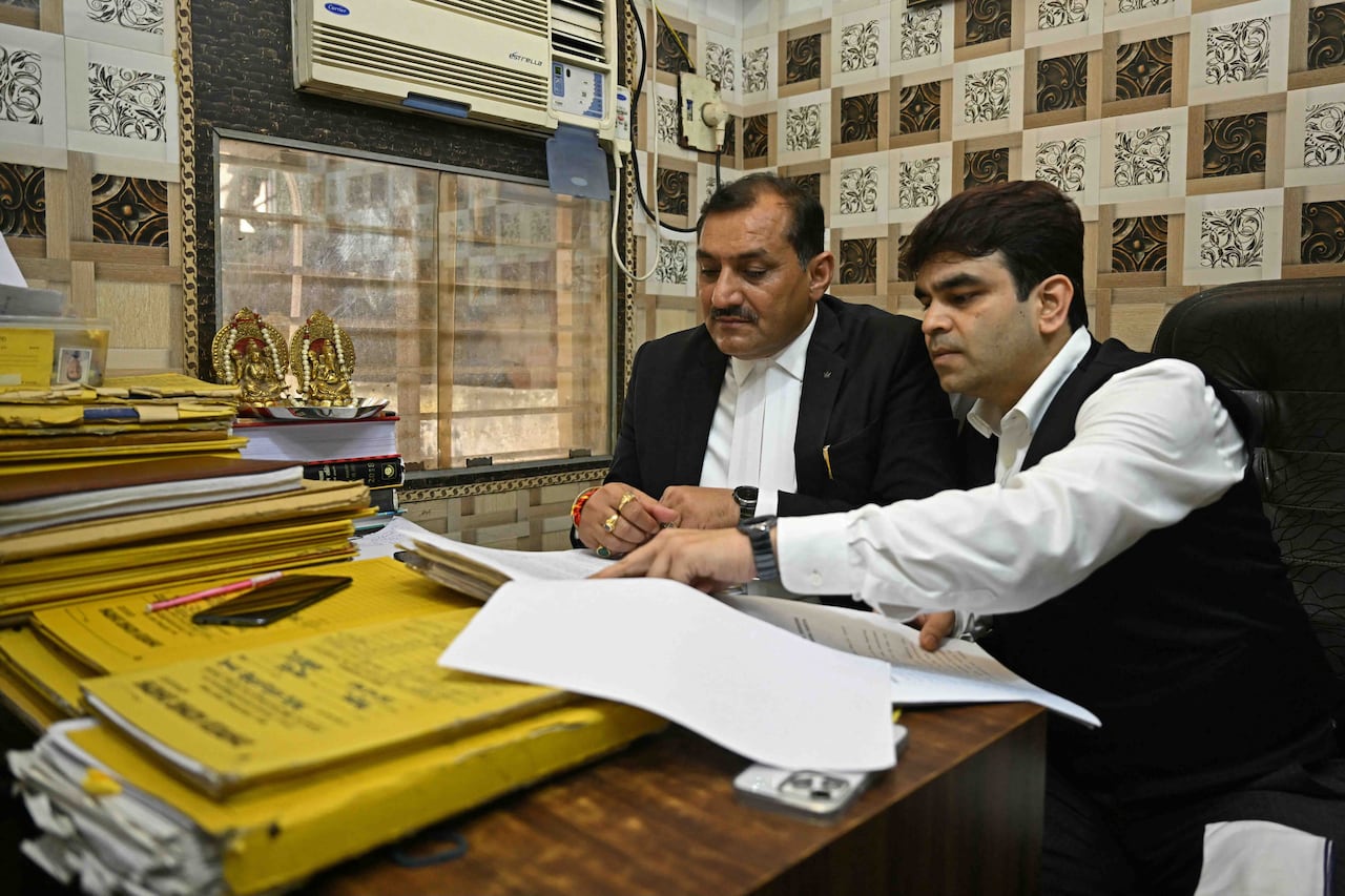 Two people sitting at a table review piles of documents in front of them.