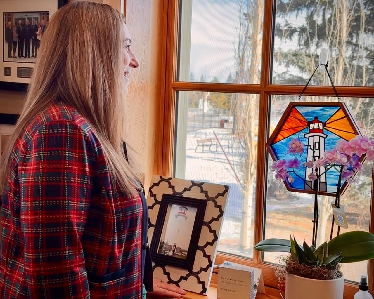 A woman in a plaid jacket looks out of her window, with photo frames on the windowsill.