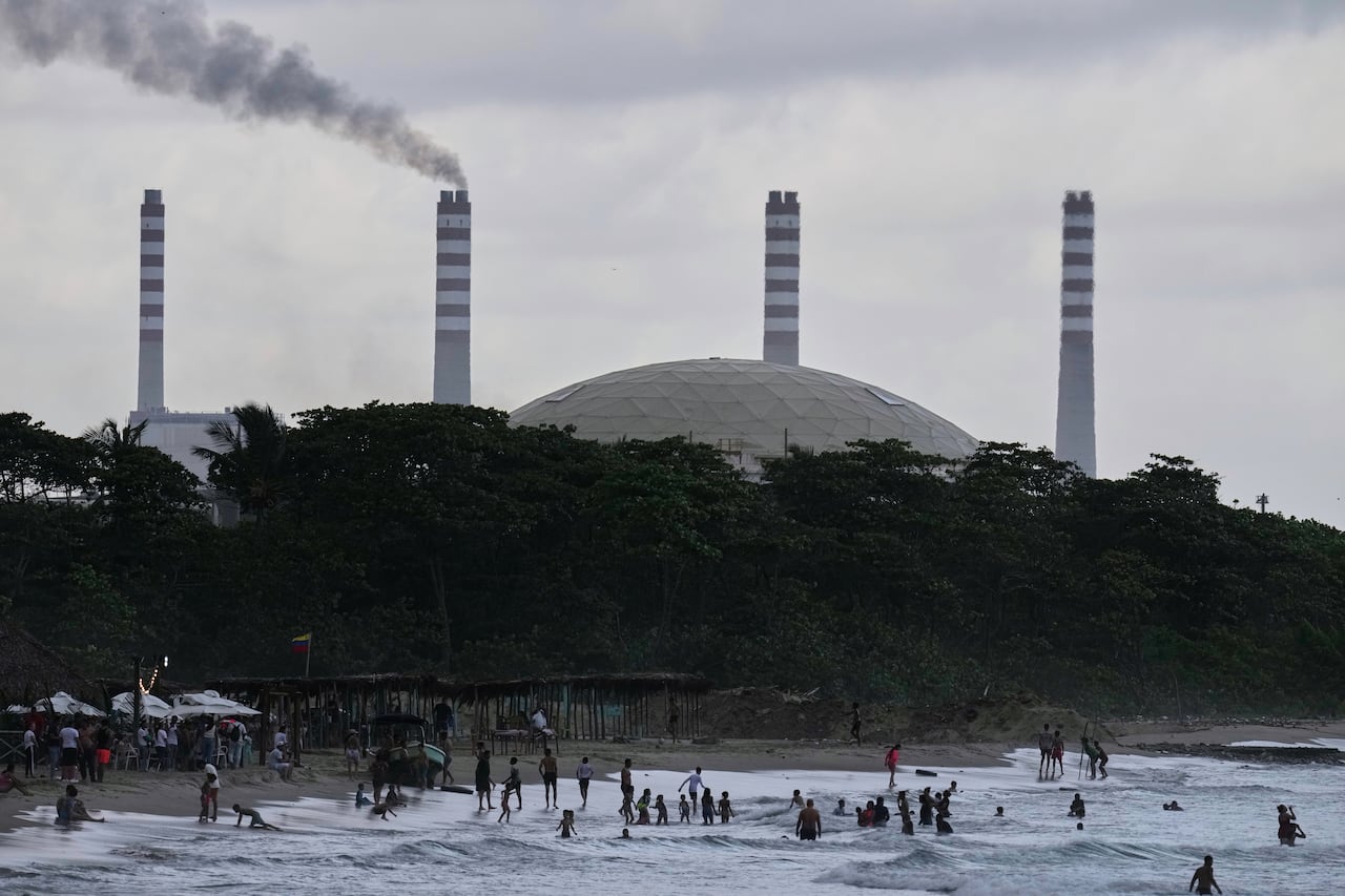 A general scene of a large refinery aside low-slung buildings with metal roofs, in a tropical climate with palm trees.