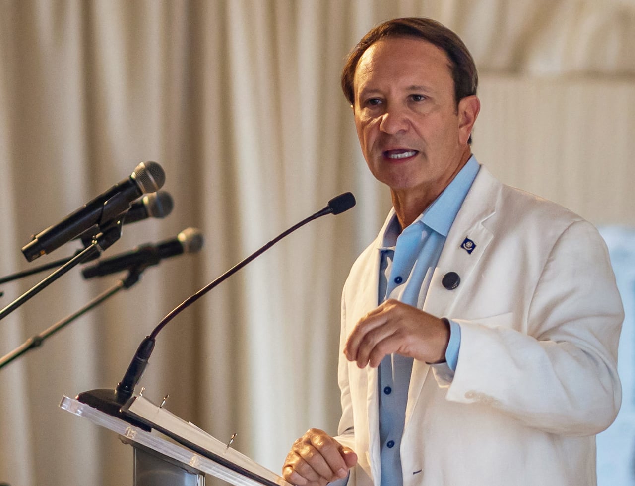 Man in light coloured suit and blue shirt speaks at a podium
