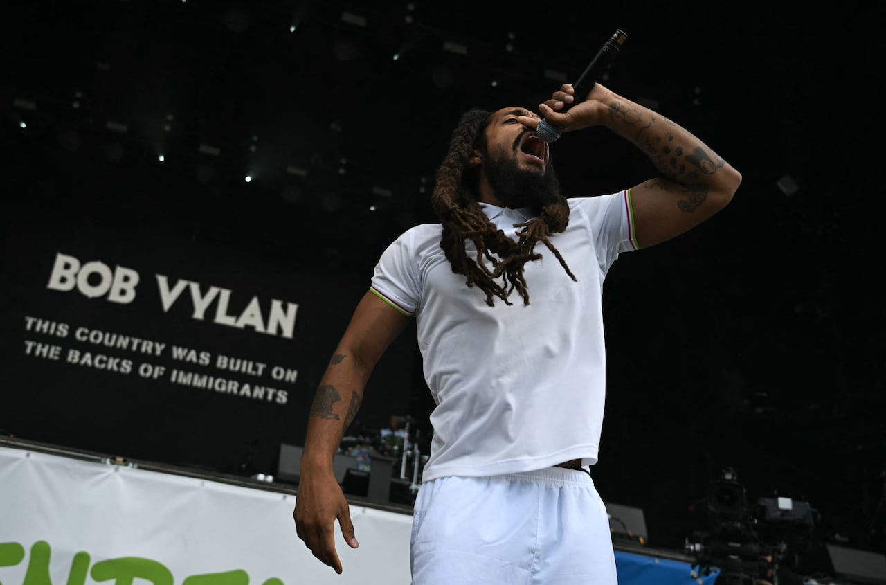 a man in all white sings into a microphone on stage 