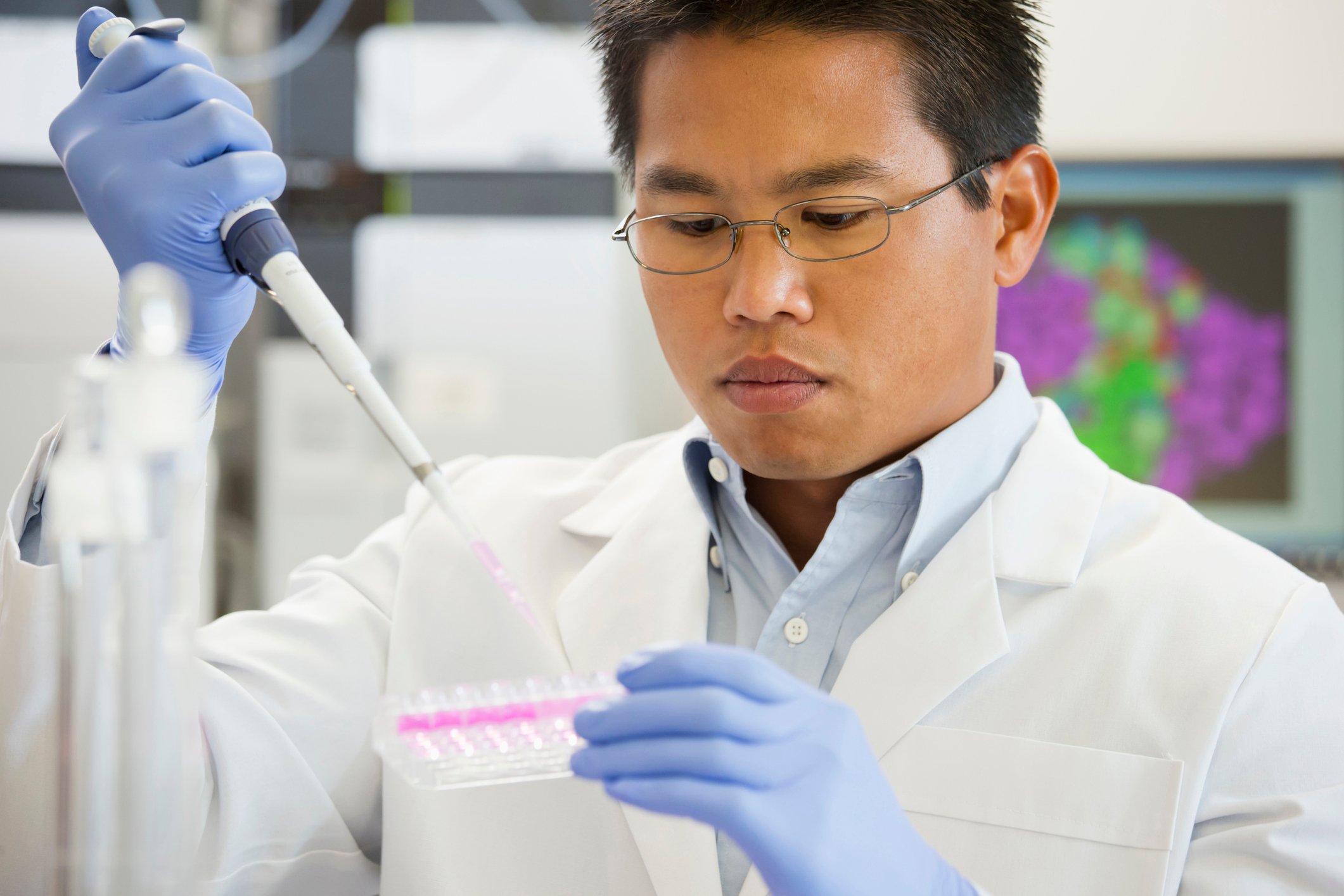 A pharmaceutical lab technician using a pipette to place liquid samples in a test tray.