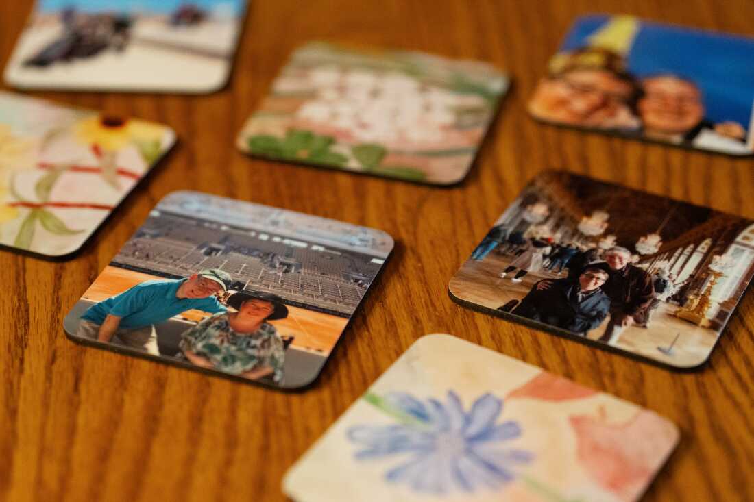 On a wood table, colorful, square drink coasters with photos of people and with artwork of flowers.  