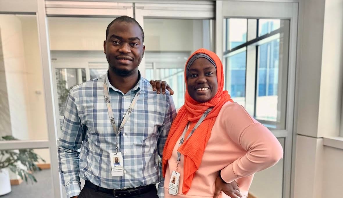 A man and woman are smiling as they stand side by side in front of a glass door.