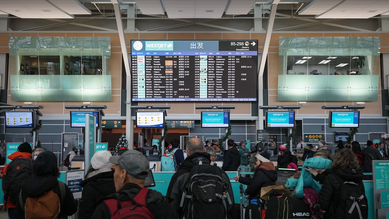 A wide shot of a busy airport terminal. Travelers with winter coats and backpacks stand in lines.