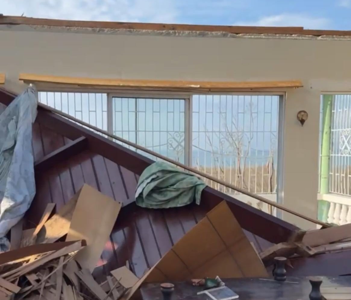 A large wooden shelf is on its side in a room with no roof, covered in broken wood.