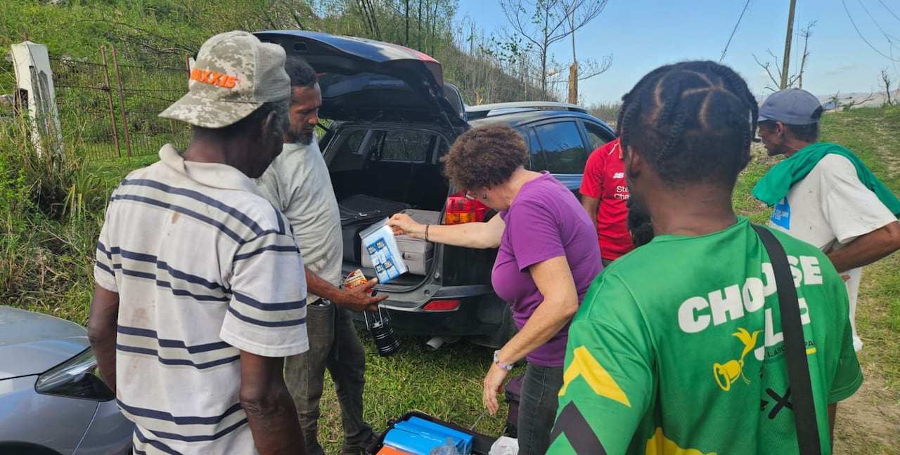 A woman hands out clothes and supplies from the trunk of an SUV