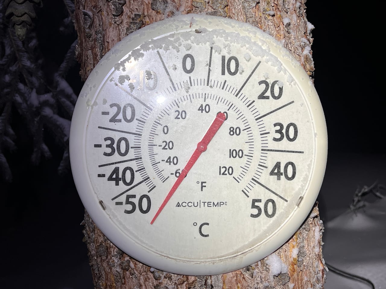 An outdoor thermometer on a tree reads a temperature below -50 C.