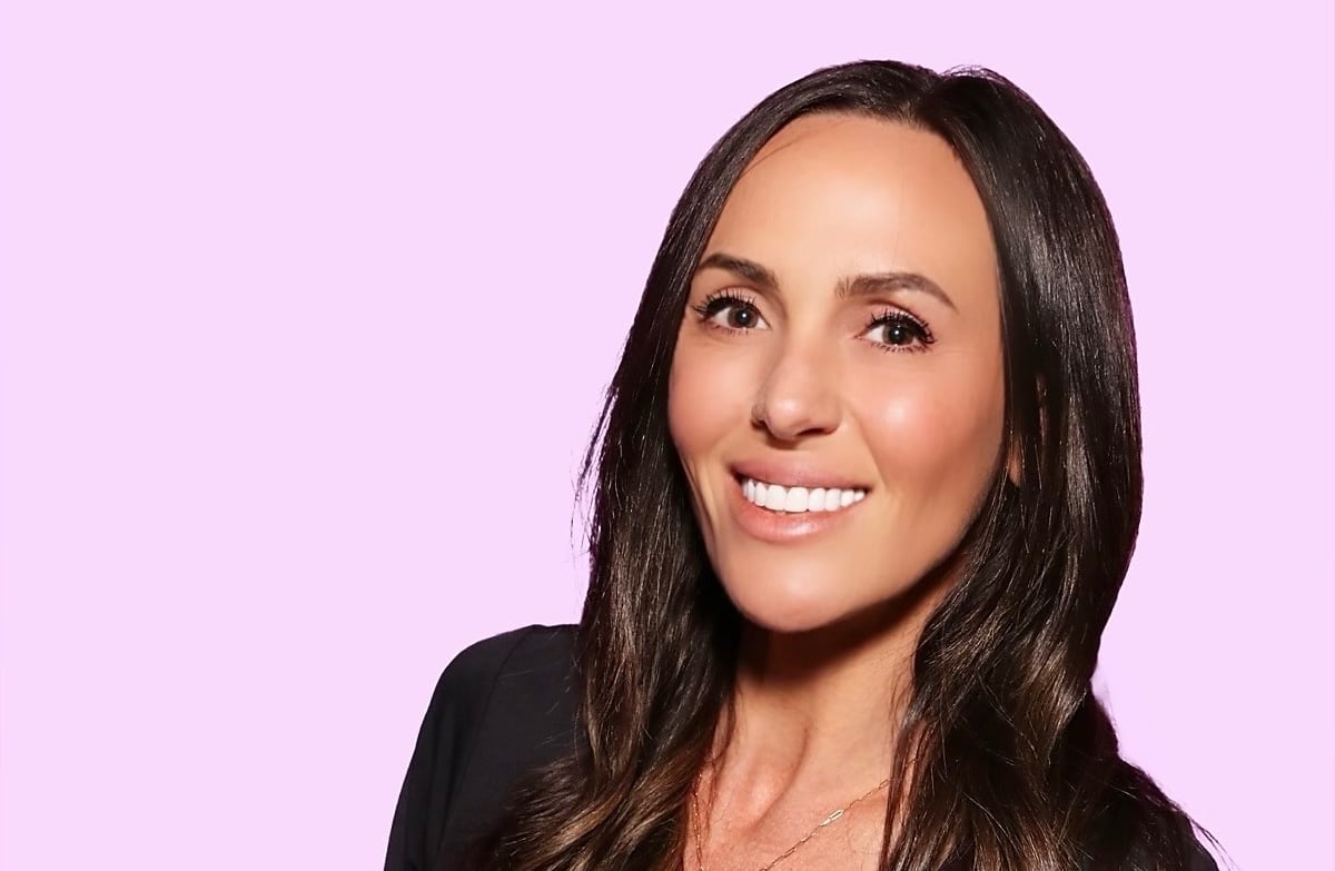 A woman smiling with a pink background behind her