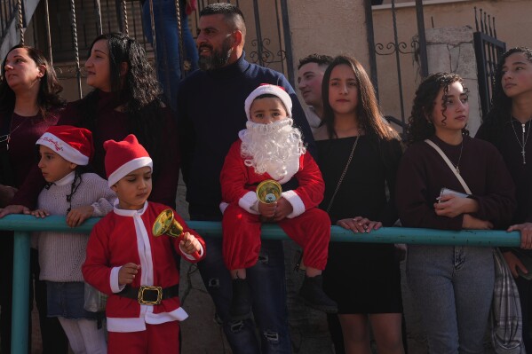 Wearing Santa Claus costumes, children watch the 40th annual Christmas parade heading towards the Basilica of the Annunciation in Nazareth, Israel, Wednesday, Dec. 24, 2025. (AP Photo/Ariel Schalit)