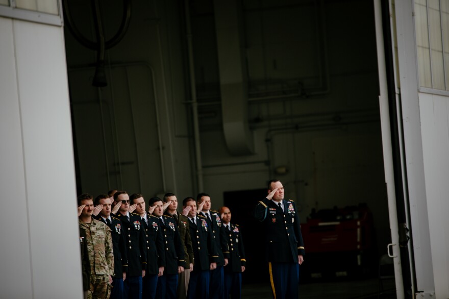 Uniformed National Guard members salute in an airplane hanger. 