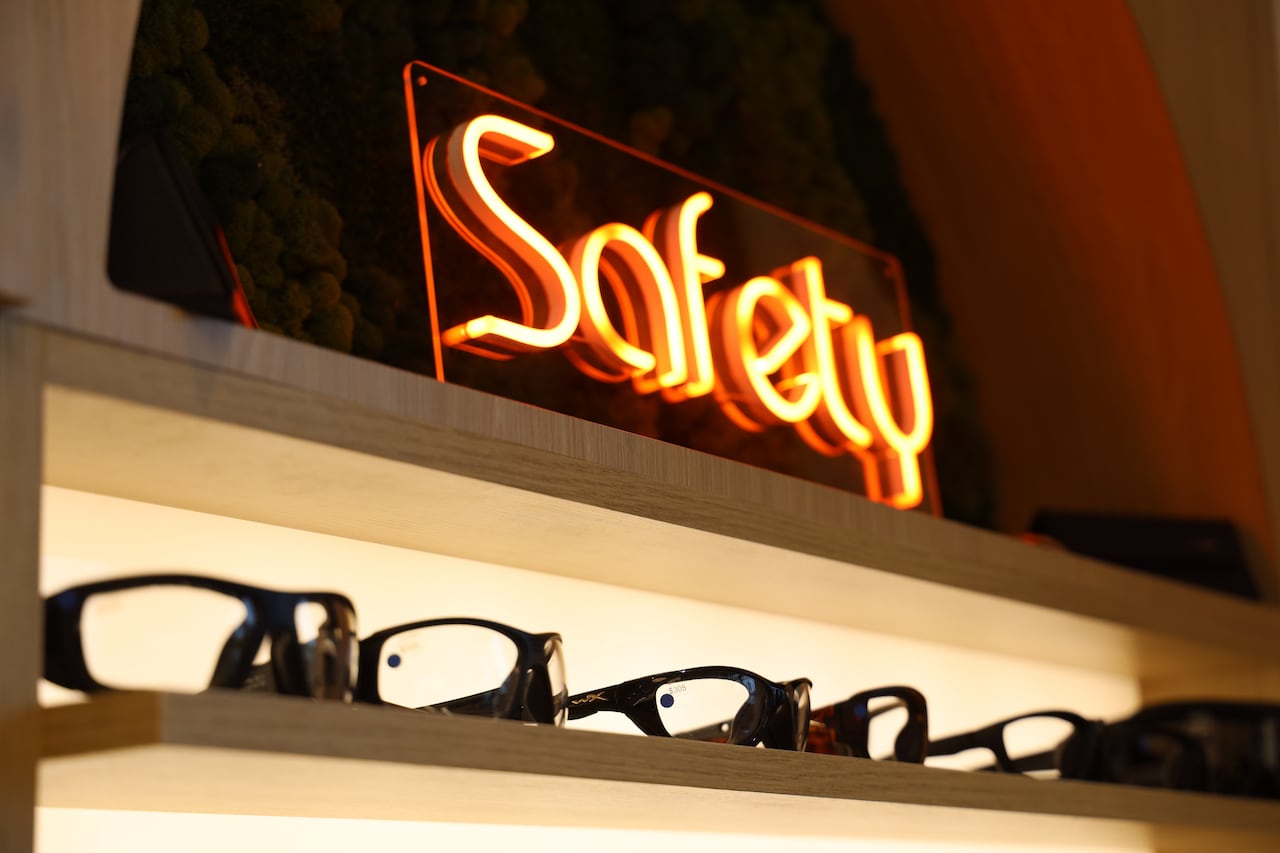 Glasses sit on a shelf below a neon sign reading "Safety."