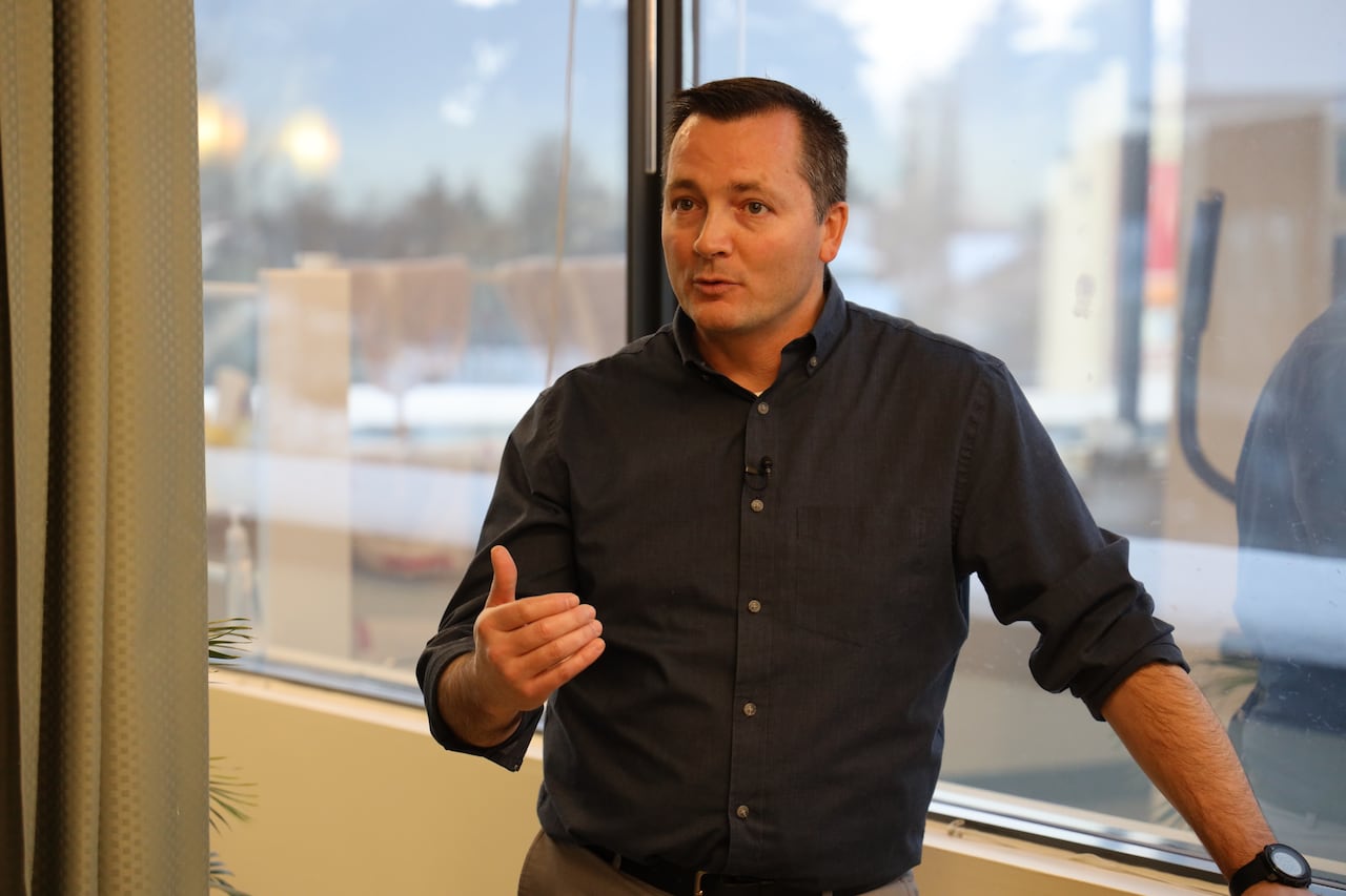 A man wearing a dress shirt stands against a window.