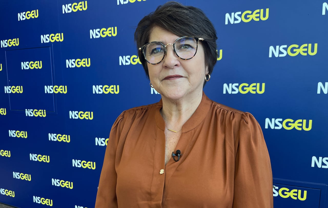 A woman with glasses stands in front of a blue sign with yellow and white letters that say NSGEU.