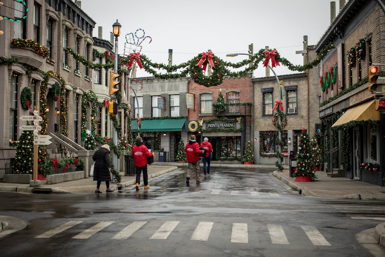 Four people carrying things walk down a street decorated for Christmas
