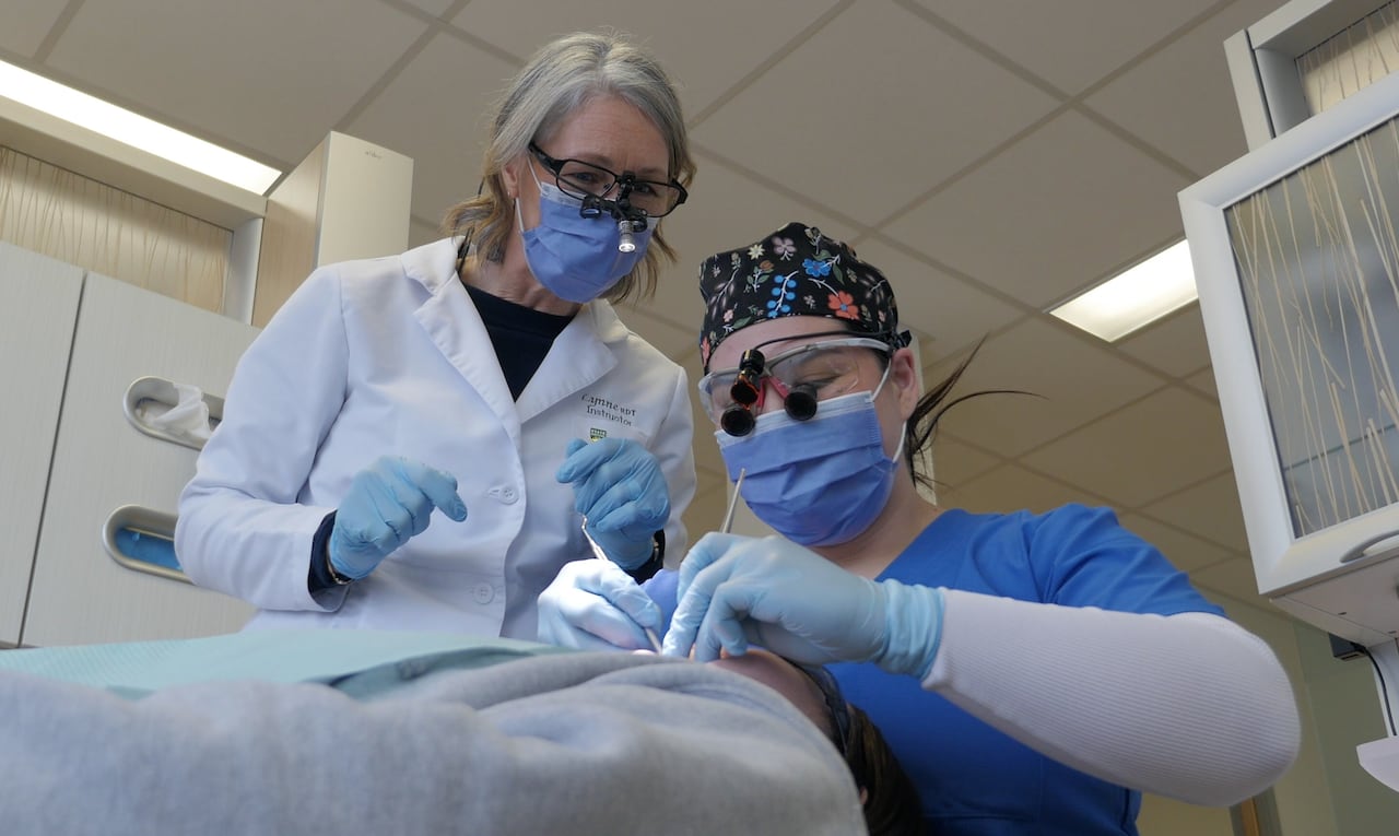A University of Saskatchewan College of Dentistry student practicing dentistry on a patient while under the watch of instructors.