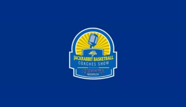 A woman in a white basketball uniform goes up for a shot while a player in an orange uniform defends