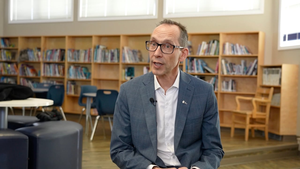 Man sitting in a library main area with chairs in the background.