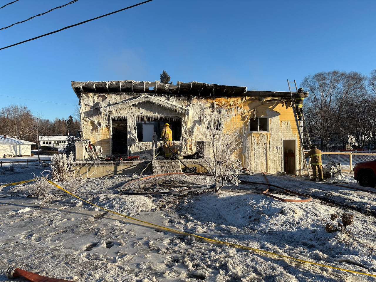 A burnt house, yellow walls, snow on the ground, firefighter scene at the door wearing yellow gear.