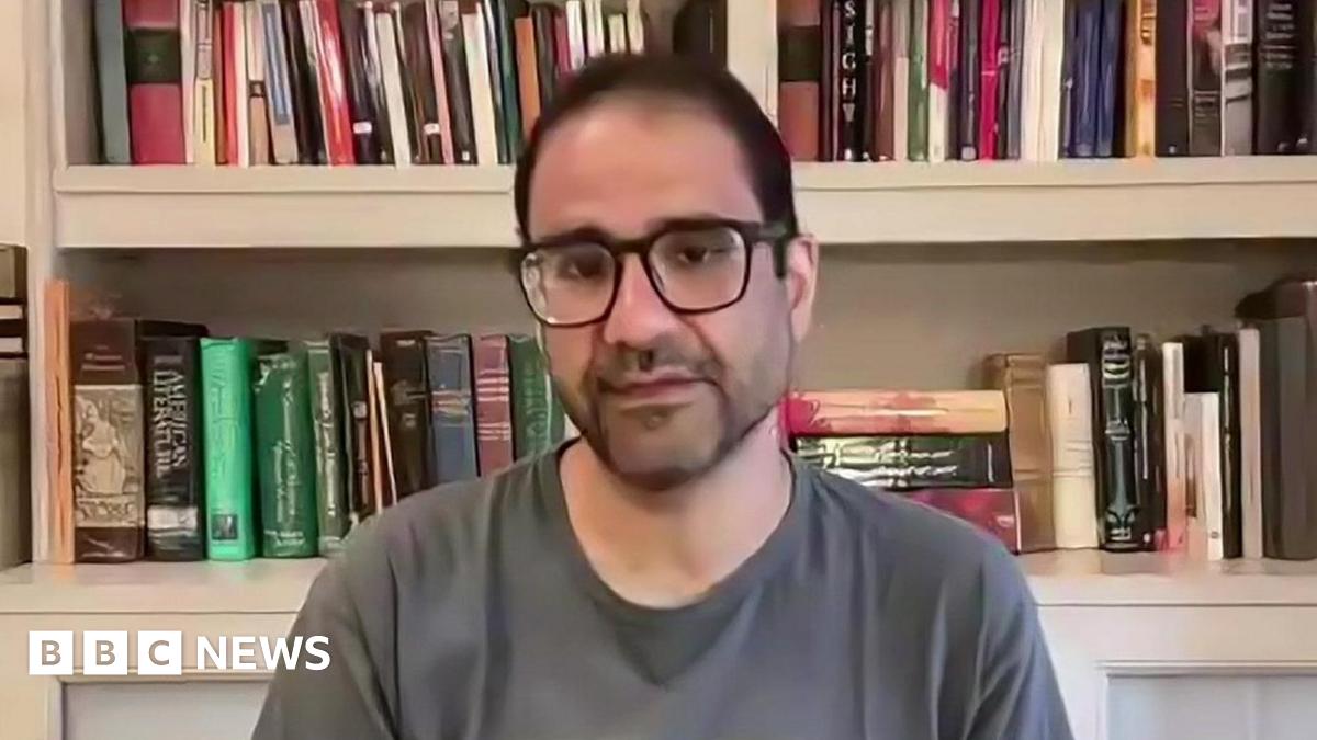 Alaa Abdel Fattah speaks via video link to the BBC in October 2025, sitting in front of a bookshelf and wearing a grey T shirt