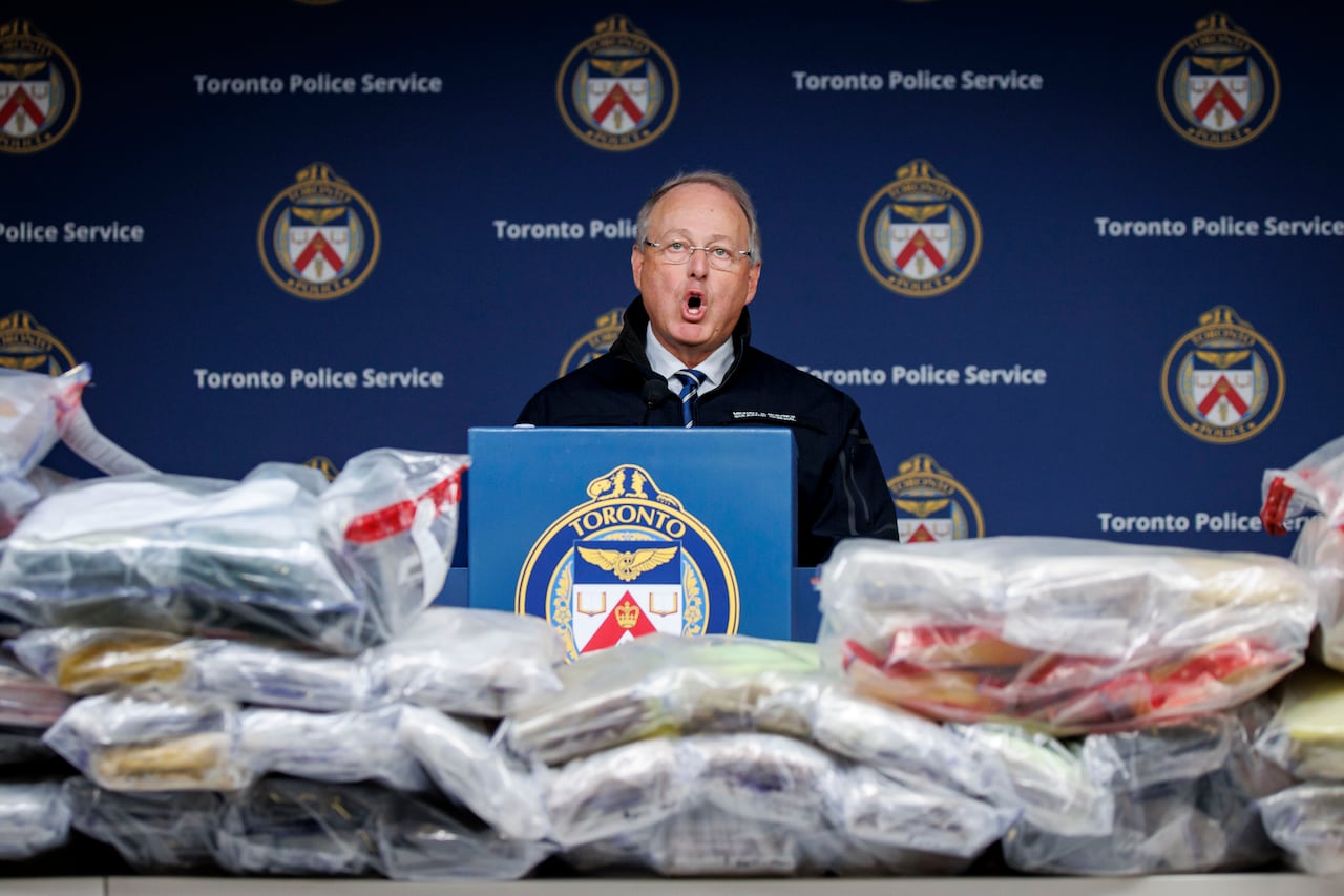 A man speaking from a podium in front of a table of seized drugs 
