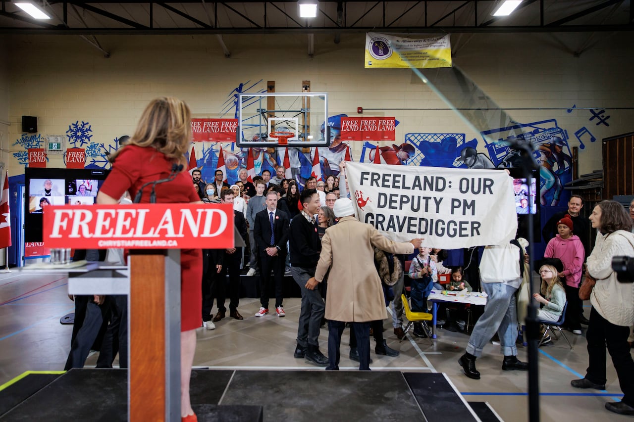 A woman in red dress standing at a podium, with supporters behind her and a commotion happening with a protester.