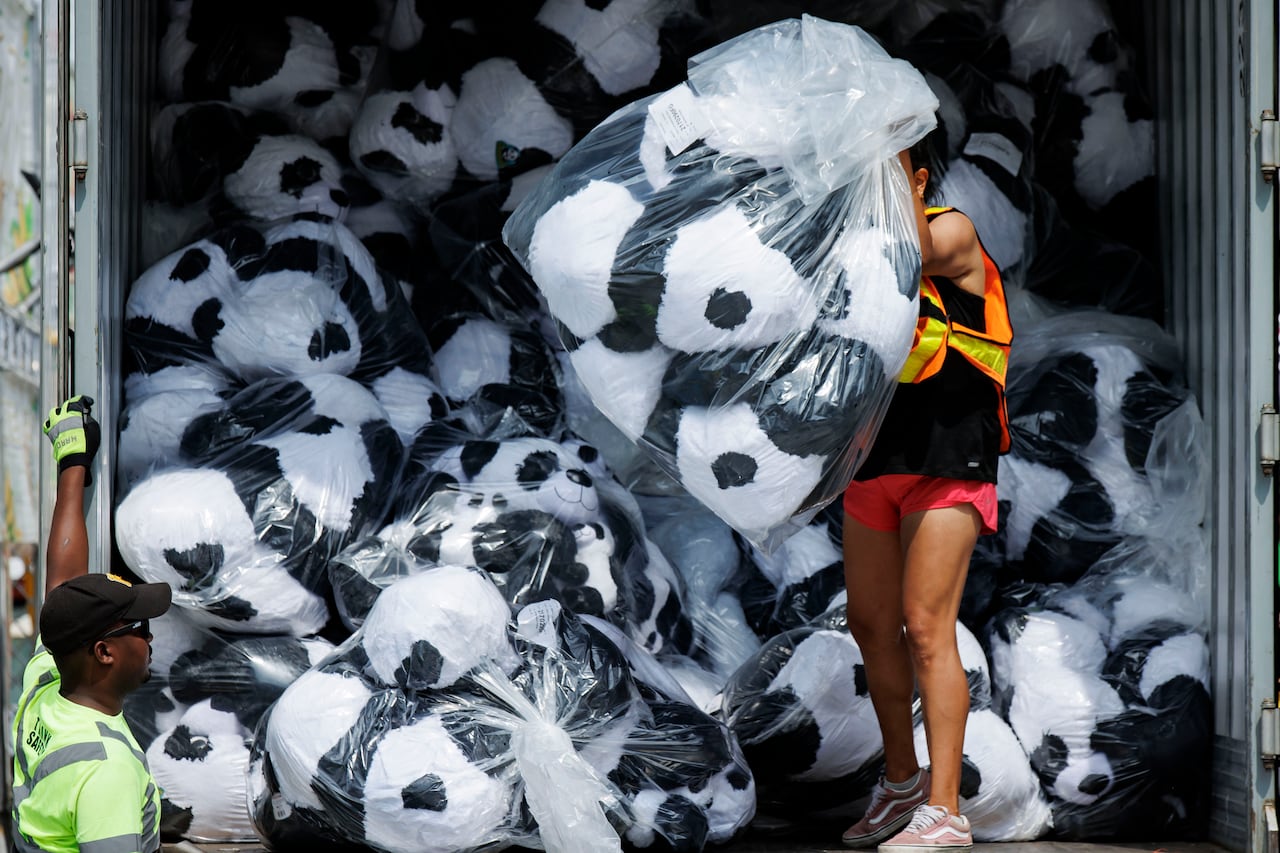 A person holding a large clear plastic bag of stuffed panda toys that are being unloaded from a truck with bags of them.