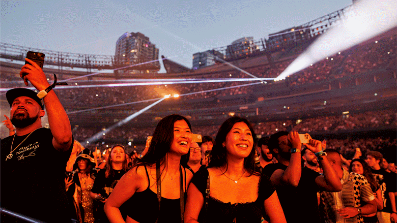 Two photos showing fans in the front row smiling amid a packed stadium, and performers on stage singing.