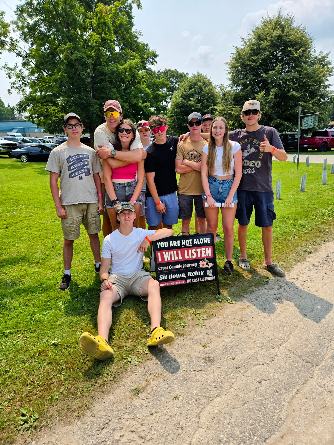 A group of young people gathered around a sign that reads 'You are not alone; I will listen.'