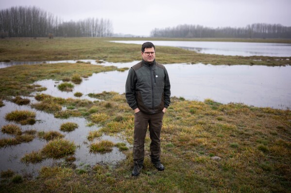 Oszkár Nagyapáti, farmer and member of the volunteer water guardians group, poses for a photo with an artificial lake in Kiskunmajsa, Hungary, Tuesday, July 29, 2025. (AP Photo/Denes Erdos)
