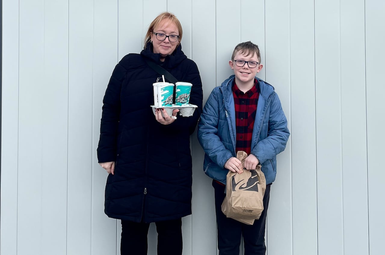 A mom and son stand in front of a Taco Bell restaurant holding bags of food