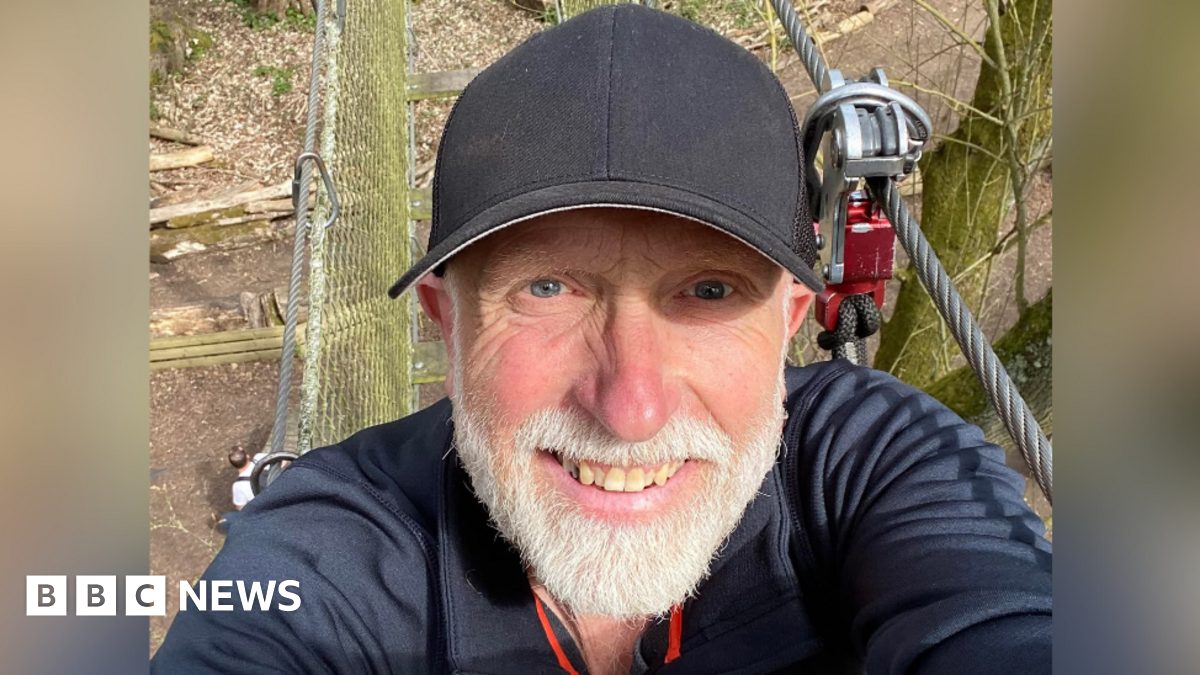 A selfie of David Darke, a 66-year-old white man wearing a sports top and a black cap. He appears to be at an outdoor activity centre.