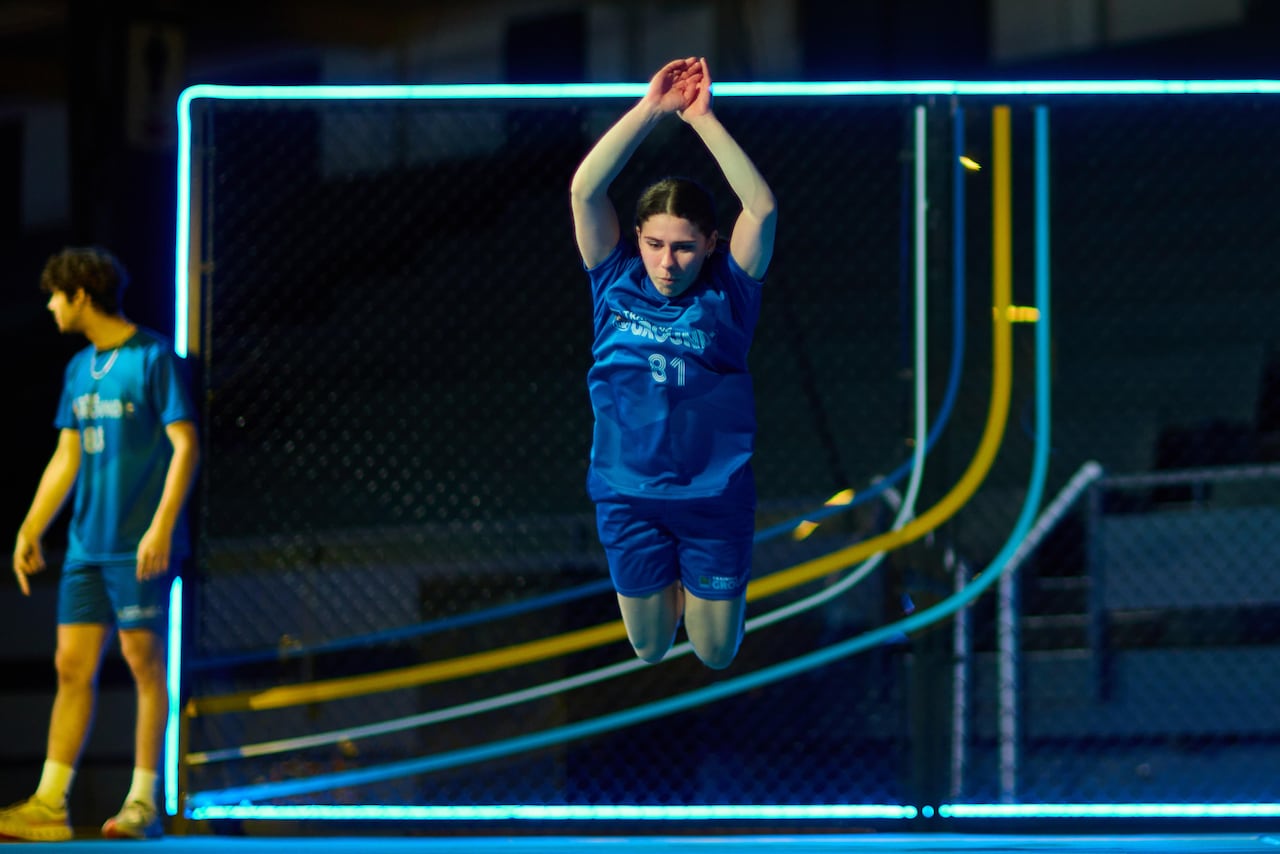 An athlete in a blue uniform performing a high vertical jump mid-air during a training session