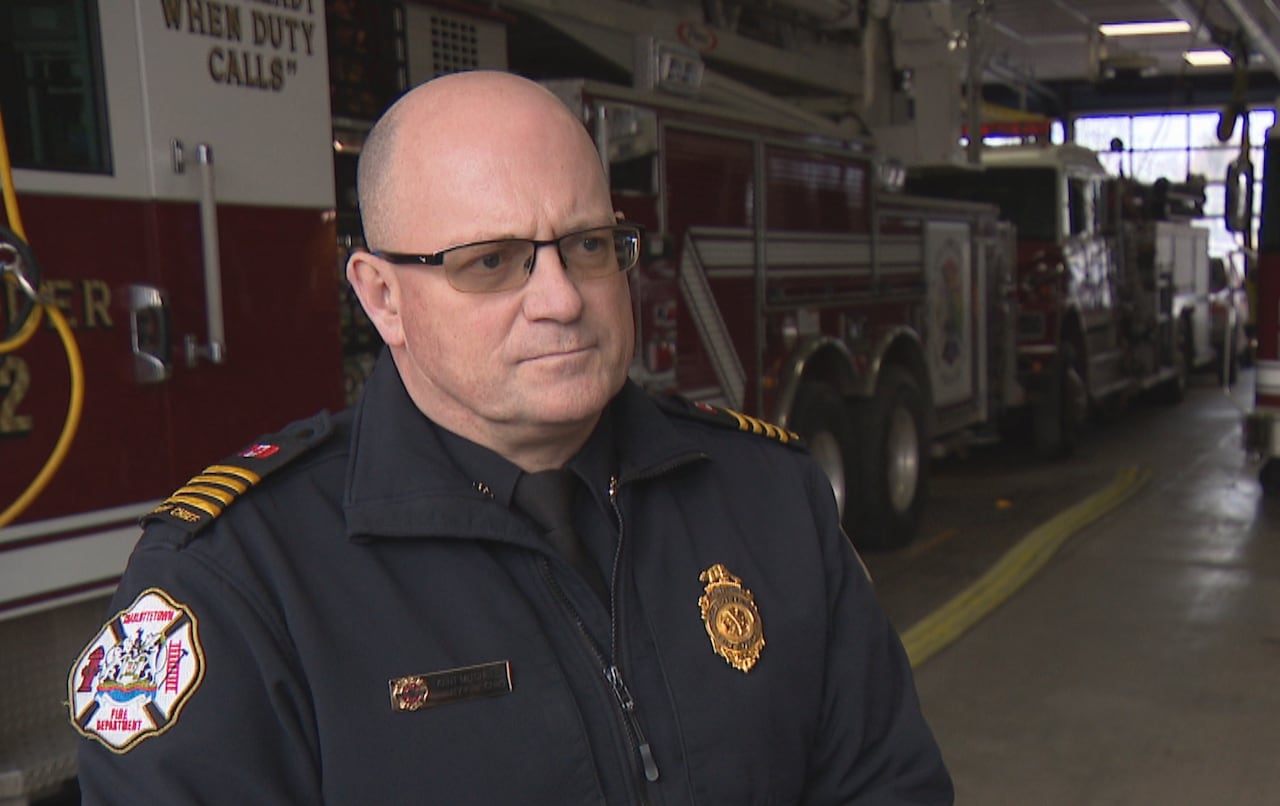 Deputy Fire Chief Kent Mitchell of the Charlottetown Fire Department stands in uniform inside a fire station with fire trucks parked in the background