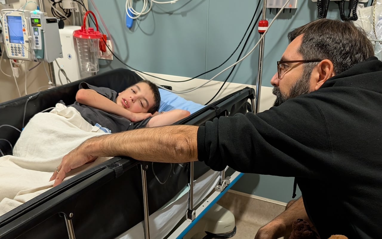 A man reaches towards a boy lying in a hospital bed.