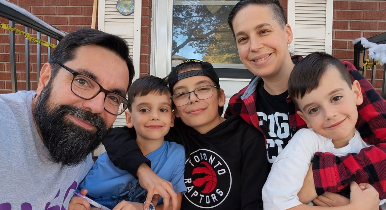 A man, woman and three children hold each other and smile for a group photo.