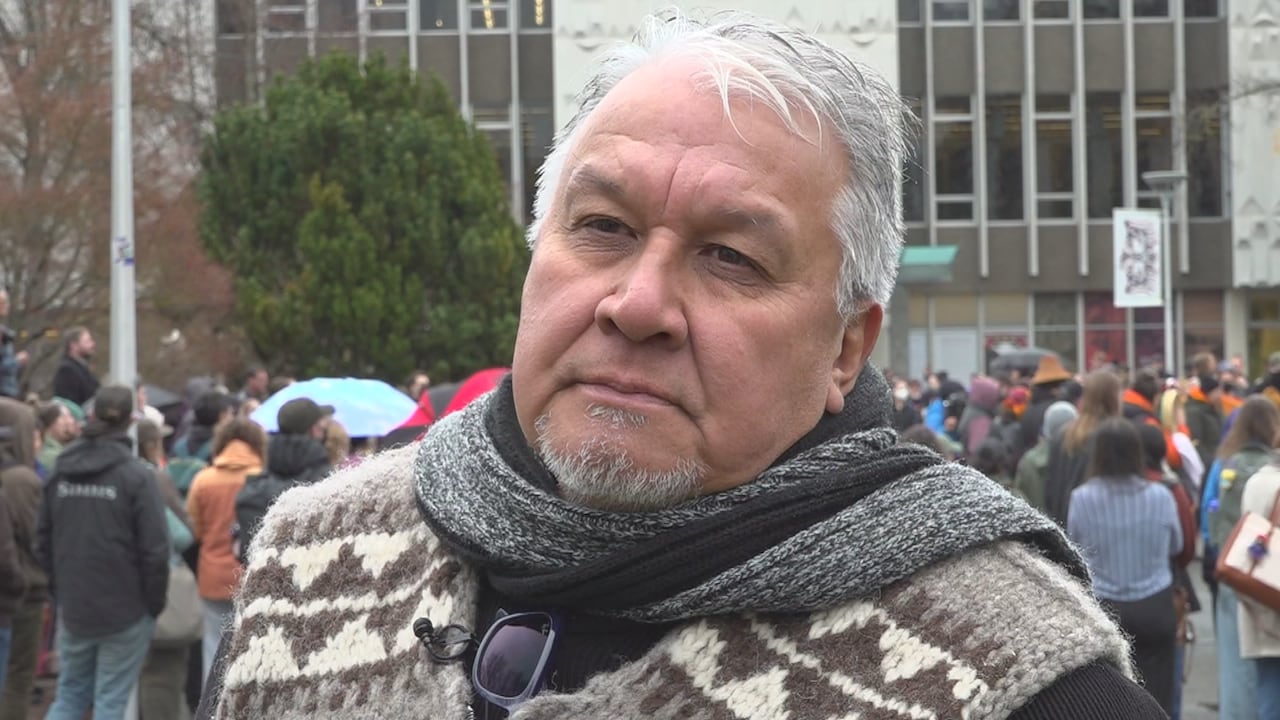 A man in a Cowichan sweater stands in front of a crowd 