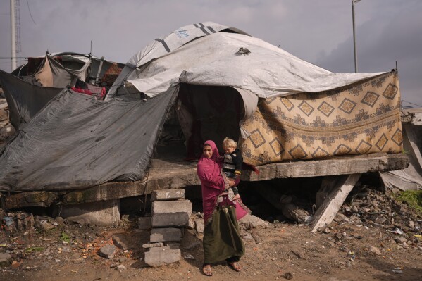 A woman holds a child as they stand in front of their tent in a makeshift camp for displaced Palestinians set up in an area in Gaza City, Monday, Dec. 29, 2025. (AP Photo/Jehad Alshrafi)