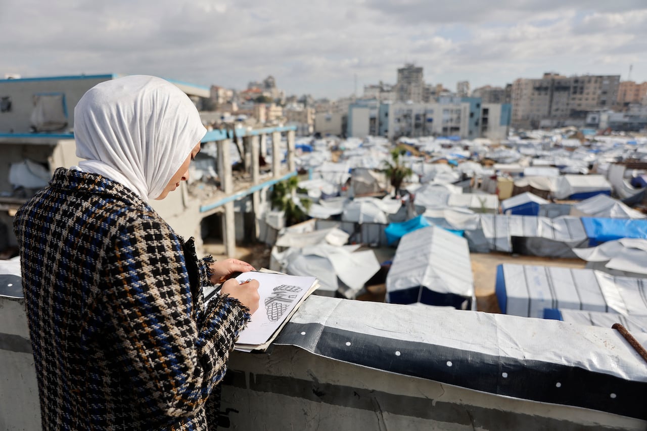 A woman stands above a tent-filled refugee camp drawing the scene in front of her